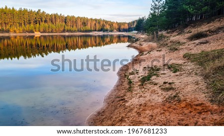 Landscape to Ogre Blue Mountain Lake and stately pine forest on a sunny day with clouds, tree reflection in the water