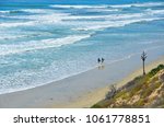 Landscape with panoramic view of two surfers walking with their surfboards, on the shoreline of Carlsbad State Beach in San Diego, Southern California.