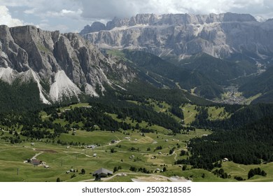 Landscape photo with a mountain range and meadow with small huts against a cloudy sky in Ortisei, Dolomites, South Tyrol region, Italy - Powered by Shutterstock