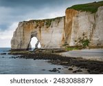 Landscape photo of tall, steep limestone cliffs by the ocean with one with a hole in it creating an arch view from the beach