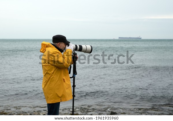Landscape photography\
in bad weather. A man in a yellow raincoat takes photos from the\
sea coast with a telephoto lens supported by a monopod. Copy space.\
                     