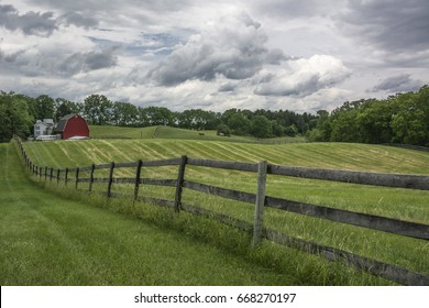 Landscape Picture Of A Farm Pasture Enclosed By Rustic Fencing With A Red Barn.