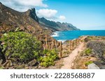 Landscape with picturesque pathway through the rocky landscape and ridges of mountain peaks. Blue Atlantic ocean waves foaming. Tenerife, Anaga National park. Unesco heritage. Roque de las Animas.