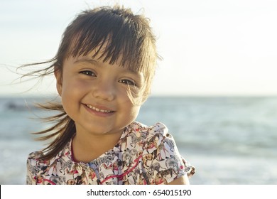 Landscape portrait of hispanic 4 year old girl sitting at the beach is looking at the camera smiling. Taken at Playa del Carmen, Mexico.