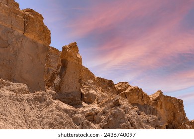 Landscape rocky formations are jagged and weathered, indicating geological changes over time. The sky is adorned with soft clouds illuminated in hues of pink and blue, creating an ethereal atmosphere. - Powered by Shutterstock