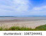 Landscape of sandy beach with rocky shore line under blue sky with cirrus clouds