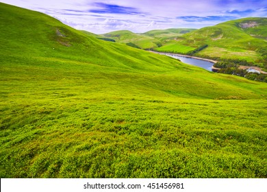 Landschaftsbild von grünem Tal, Hügel, Fluss und bewölktem blauen Himmel. Pentland-Hügel, Schottland