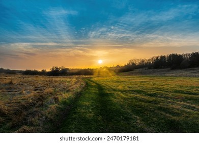 Landscape with the setting Sun over a meadow with a dirt country road. Picturesque nature and sunset - Powered by Shutterstock