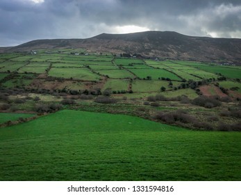 Landscape Shot Of Farmland In Southern Ireland - With A Valley In The Foreground, And Mountains In The Background
