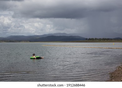 Landscape Shot Of A Man In A Rubber Ring On A Lake Watching A Storm Approaching