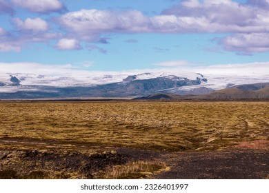 Landscape showing the contrast between fire   ice  Lava field and snow capped mountains in the background under blue sky