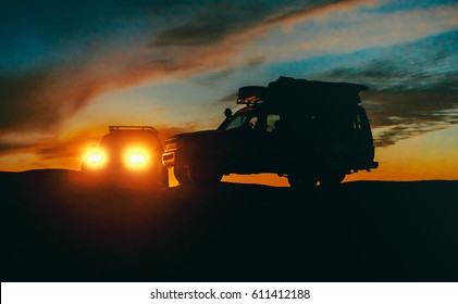 Landscape with silhouettes of two off-road cars at sunset, low light photo. Traveling by car - idea for your adventure in wildlife, scientific expedition or extreme travel on a SUV automobile.