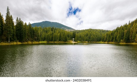 landscape of a synevyr lake in spring. scenery with fir forest on the shore and hills. beauty of carpathian mountains
