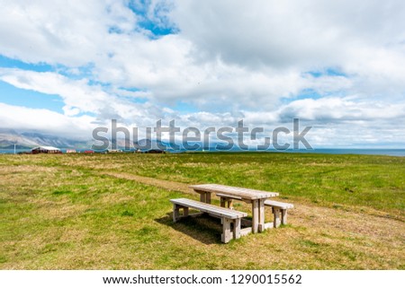 Landscape trail hiking view of Hellnar National park Snaefellsnes Peninsula in Iceland with town and green grass in summer day wooden picnic table and nobody