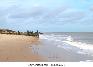 Landscape of vast sandy beach with gentle ocean waves and view of vast sand with wood sea defence barrier in distance with no people on deserted shore on  tranquil day in Norfolk East Anglia England 
