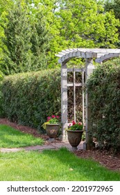 Landscape View Of An Arched Wooden Arbor Trellis In An Ornamental Botanical Garden Surrounded With Green Grass And Shrubbery
