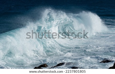 Landscape view of blue rolling wave slamming on volcanic stones of the coastline like a tsunami. Beautiful spray due to the wind. Costa Teguise, Lanzarote, Canary Islands, Spain.	
