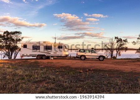 Landscape view of a a large white caravan and modern 4WD vehicle at a free camp next to the nearly dry salt Lake Norring near Wagin in Western Australia in late afternoon sunshine.