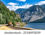 Landscape view of  the locomotive pulls a train of freight cargo wagons on a railroad along Columbia River in Columbia Gorge scenic area with mountain ranges with evergreen trees along the river