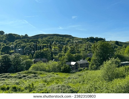 Landscape view over, fields, houses, and trees, with distant hills, set against a hazy blue sky in, Walsden, Todmorden, UK