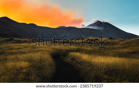 Landscape view of a path trail on the Mount Etna volcano during a lava eruption with smoke at sunset