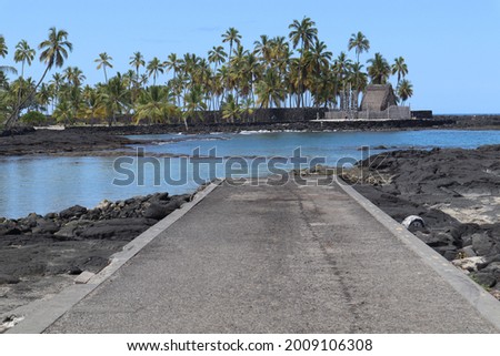A landscape view of a slipway on the black volcanic rock beach, with palm trees in the background on the Hawaiian Island of Kona