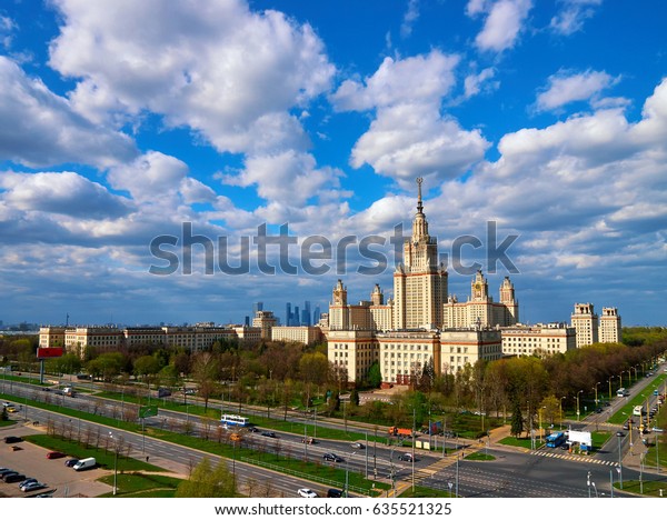 A landscape view of the\
sunny spring campus of Lomonosov Moscow State University under blue\
cloudy sky
