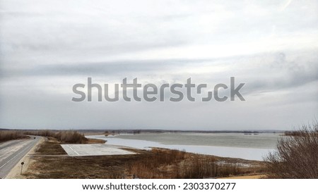 Landscape with the water of lake, river, bay or reservoir with gray water, gloomy sky and clouds and the shore on an autumn, spring or winter day. View from a height