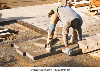 Landscape worker paving driveway interlock patio with stone brick at construction site. Contractor wearing safety protective cloth, gloves and knee pads for heavy installation yard work project.