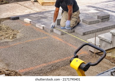 Landscaping contractor worker using tape measure ruler measuring and laying interlock stones on a construction site.