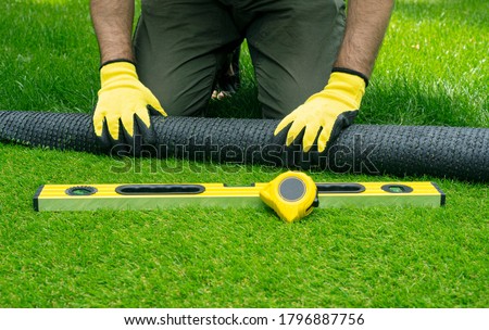 Landscaping of the yard with artificial turf. Gardener hands hold a roll of artificial grass.