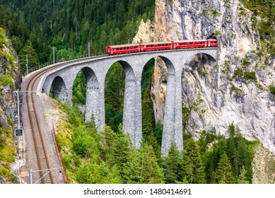 Landwasser Viaduct in Filisur, Switzerland. It is a famous landmark of Swiss Alps. Red express train on high bridge in mountains. Scenic view of amazing railway in summer. Concept of travel in Europe. - Shutterstock ID 1480414691