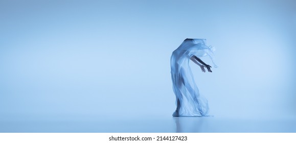 Language of body. Young flexible woman, graceful ballerina dancing with fabric, cloth isolated on blue studio background. Grace, art, beauty, contemp dance, ad concept. Monochrome