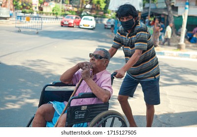 Lansdowne, Kolkata, 04/09/2020: A disabled senior adult wearing black spectacle (either due to blindness or low vision) in a wheelchair is being cared by a middle aged person in street. 