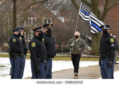 Lansing, Michigan, U.S. January 17, 2021. Man carrying a "blue stripe" American flag signifying support for police on the lawn of the Michigan capitol, approaching Michigan State Police officers.