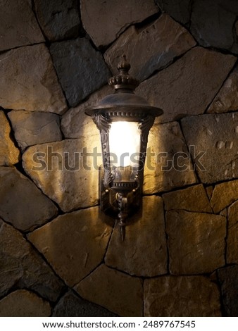 Lantern with flame in retro style on the background of a stone wall of an ancient house.