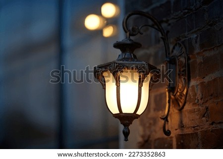 Lantern light on wall of building at night. Vintage european design lantern hanged on wall at night. Street lantern wall mounted, yellow warm light in evening. 