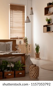 Lantern And Plants In Dark Bedroom Interior With Bed Next To Lamps And Blinds On Window. Real Photo