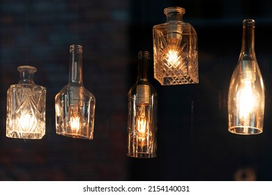 Lanterns made of glass bottles and Edison lamp bulbs. DIY lamps made from recycled old bottles hanging in cafe window - Shutterstock ID 2154140031