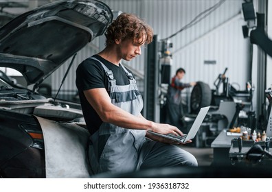 With laptop. Adult man in grey colored uniform works in the automobile salon.