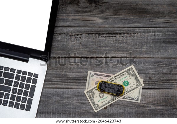 Laptop against\
the background of a gray wooden table next to an overturned toy car\
on dollar bills. Flat lay, top view. Concept of online insurance,\
automobile repair,\
accident.