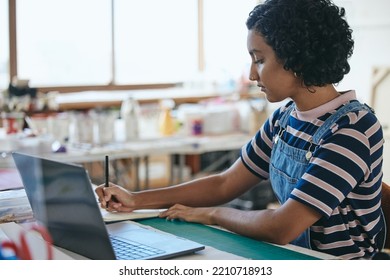 Laptop, Art And Education With A Woman Student In A Creative Classroom, Workshop Or Studio While Writing In A Notebook. Computer, Learning And School With A Female Artwork Pupil Studying In Class