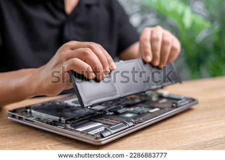 Laptop basic service of battery replacement, Technician Man holding the new battery and insert in the computer to repair laptop and remove the old part on the table to wait for removal, service work