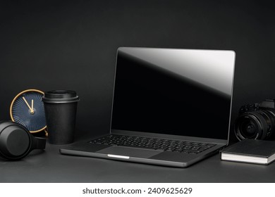 Laptop with black screen on working desk with cup and earphones on black background - Powered by Shutterstock