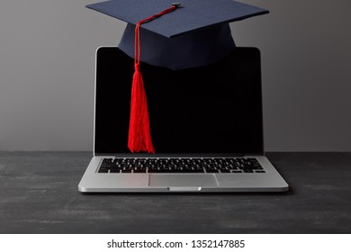 Laptop With Blank Screen And Academic Cap With Red Tassel On Grey