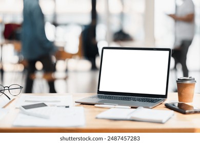 A laptop with a blank screen, coffee cup, and office supplies on a wooden desk in a modern open office setting with blurred background. - Powered by Shutterstock