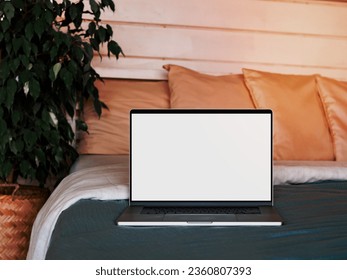 Laptop blank screen on bed in country house bedroom interior background, mockup, template. Clipping path device screen. Silver aluminium laptop at bed near green waringin tree