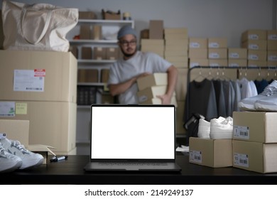 Laptop With Blank White Screen Standing On The Desktop In The Warehouses. E-commerce Business Owner Working In Store Warehouse.