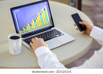 Laptop with business chart, cup of coffee and a man with smartphone