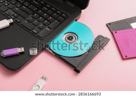 Laptop with CD disk and different memory storage devices on pink background